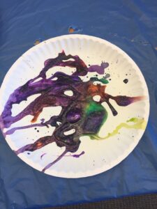 a paper plate with mixed swirls of purple, orange, green, and yellow, paint